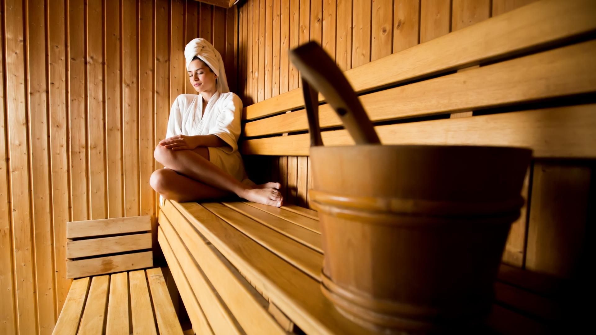 Relaxed woman in wooden sauna with bucket and ladle.