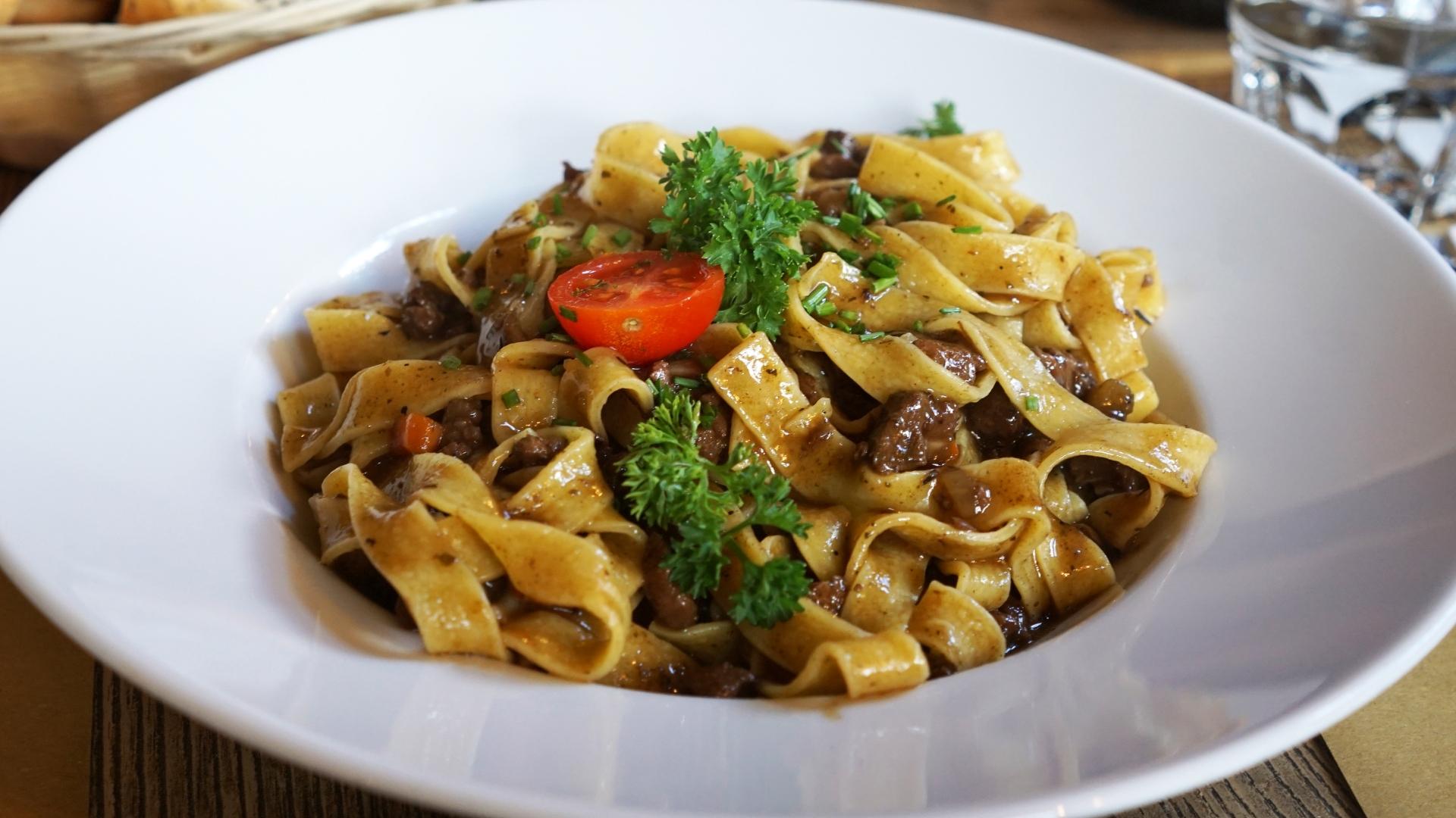 Tagliatelle with meat sauce, garnished with parsley and cherry tomato.