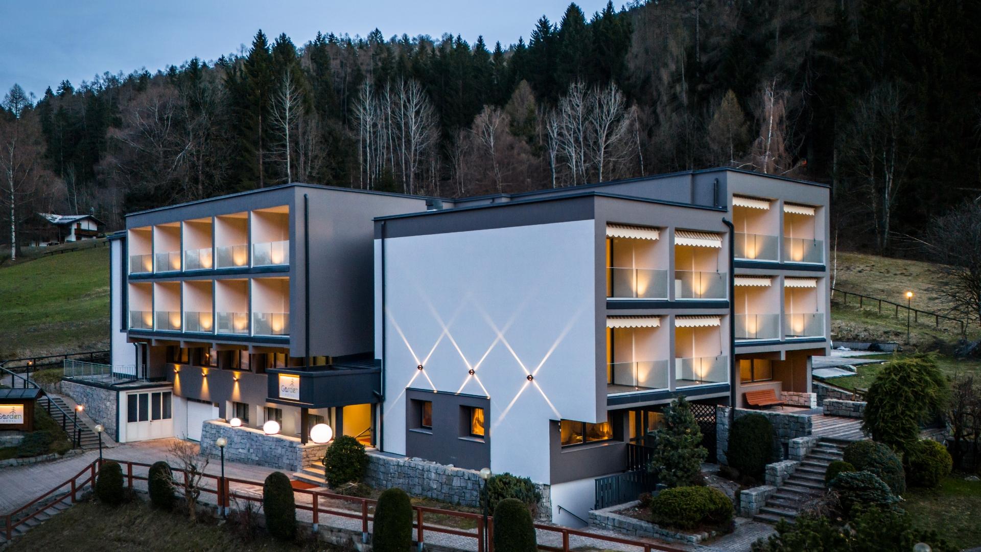 Modernes Hotel in der Natur, mit beleuchteten Balkonen und Blick auf die Hügel.