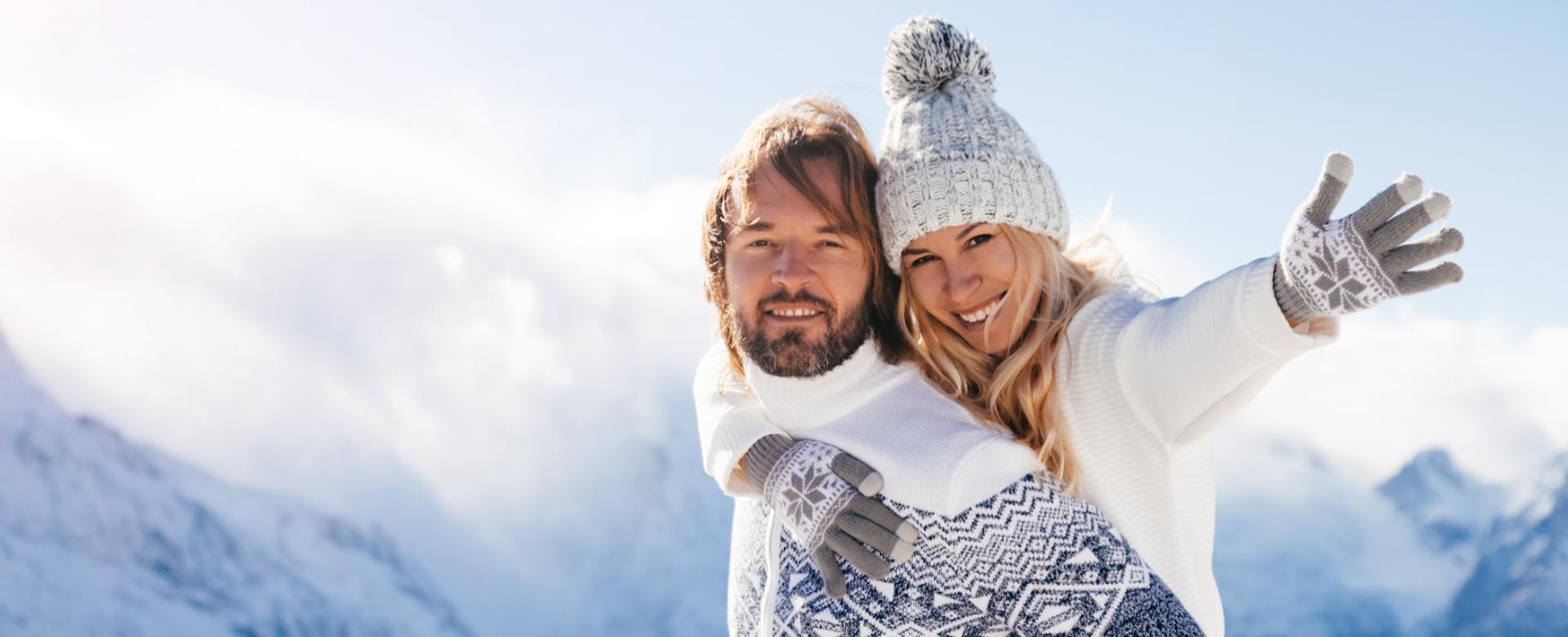 Coppia felice in montagna con abbigliamento invernale, cielo azzurro e neve.