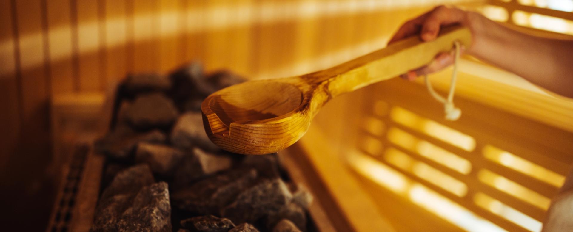 Person pouring water on hot sauna stones with a wooden ladle.