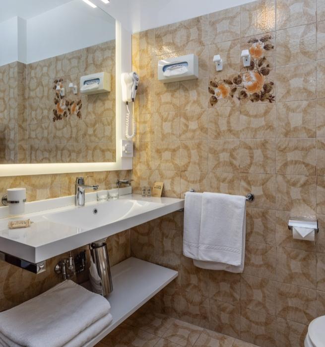 Bagno moderno con specchio illuminato, lavandino bianco e piastrelle beige decorate.