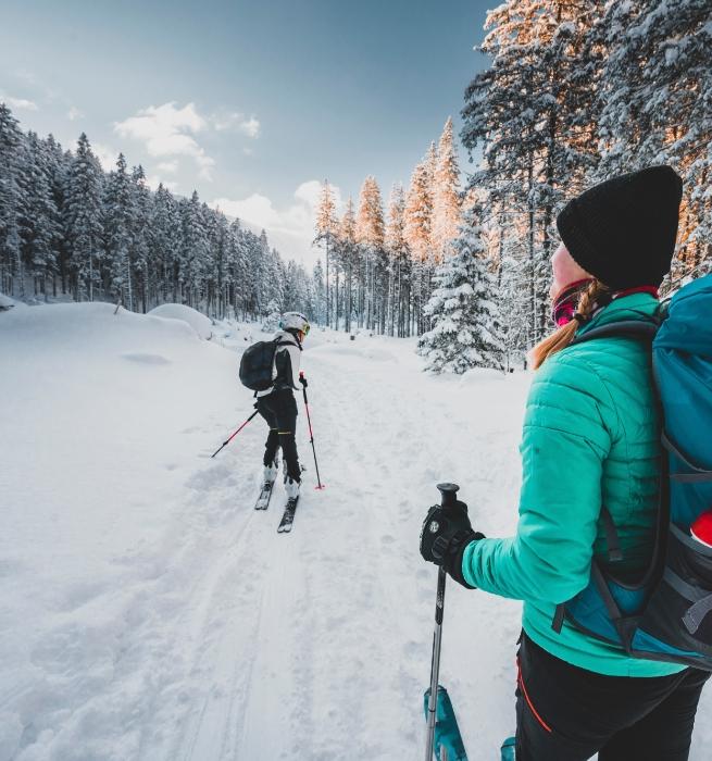 Zwei Personen fahren bei Sonnenuntergang durch einen verschneiten Wald Ski.