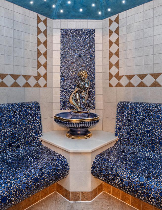 Relaxation room with blue benches, mosaics, and a central decorative statue.