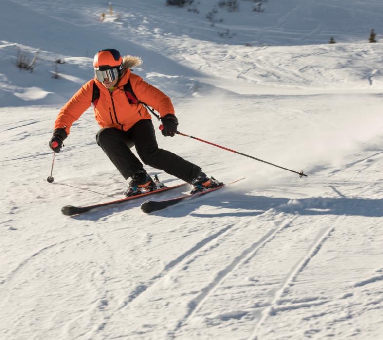 Skier descending a snowy slope in orange clothing.