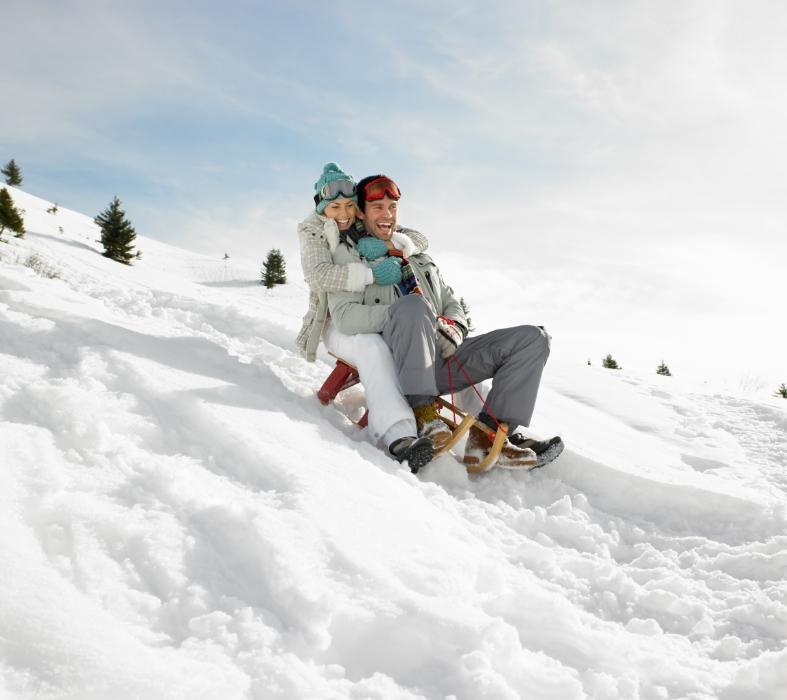 Happy couple sledding on the snow on a sunny day.