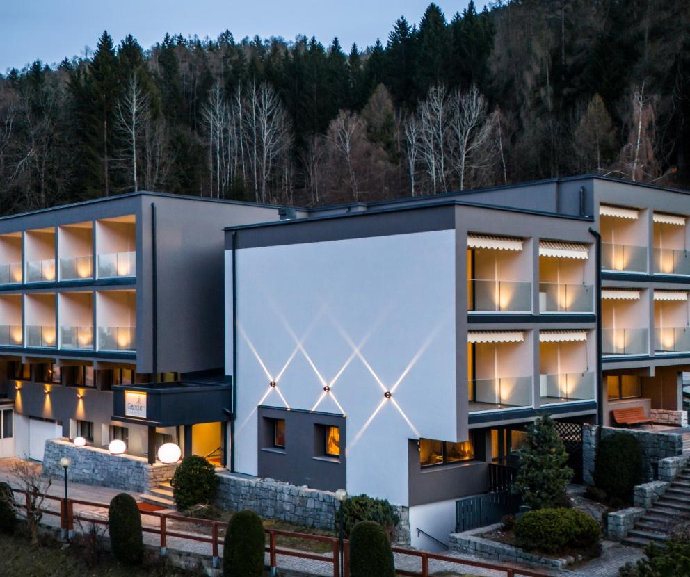 Modernes Hotel in der Natur, mit beleuchteten Balkonen und Blick auf die Hügel.